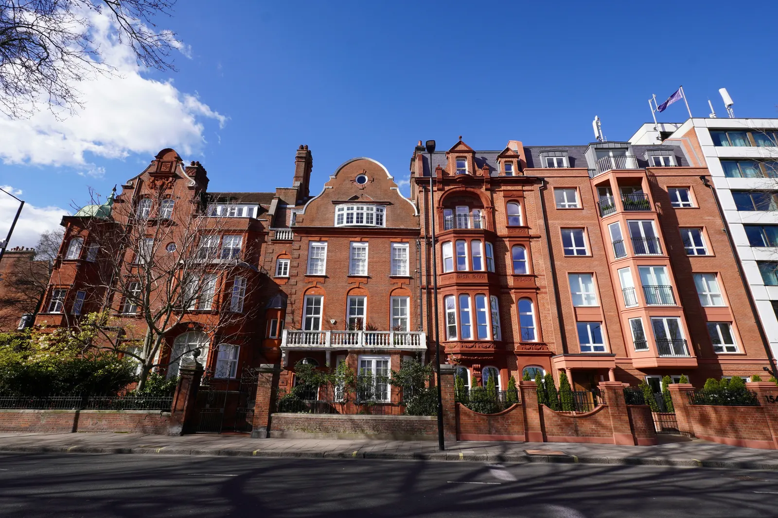 A terrace of red-brick mansion blocks on a London street under a blue sky